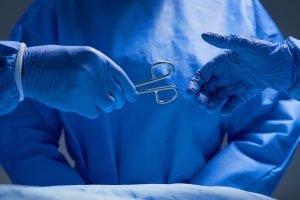 Deux mains gantées de chirurgiens se donnant un ciseau chirurgical.