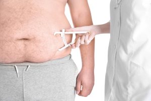 Un professionnel de la santé portant une blouse blanche, entrain de mesurer la graisse du ventre d'un homme avec un étrier de couleur blanc.