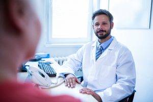 Un médecin portant une blouse blanche assis à son bureau. Devant lui sont posés un téléphone et le clavier d'un ordinateur.